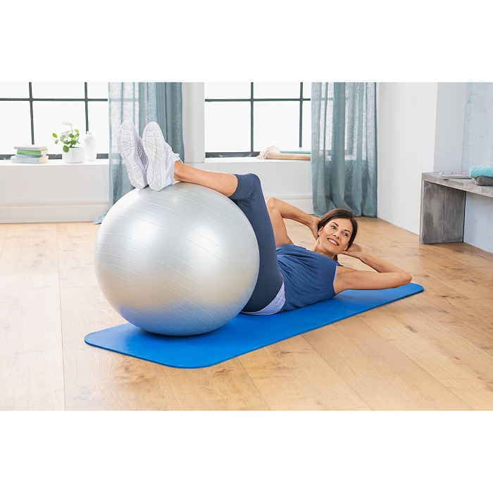 Eine Frau liegt auf dem Rücken auf einer Fitnessmatte. Unter ihren Beinen ist ein silberner Gymnastikball.