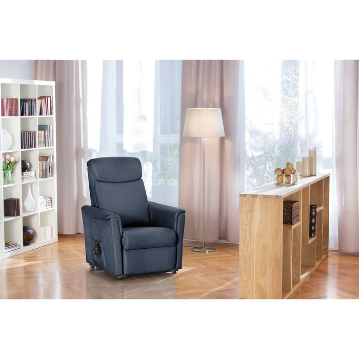 Ein titanfarbender Sessel in einem Wohnzimmer. Er steht relativ zentral. Ebenfalls ist ein Bücherregal und ein hüfthohes Holzregal zusehen.